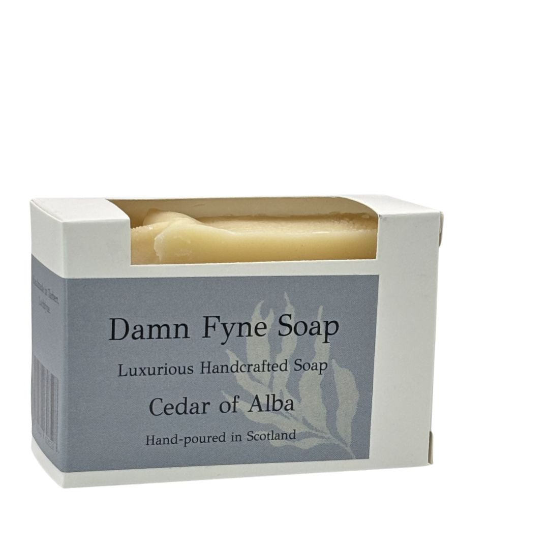 Cedar of Alba soap bar in biodegradable kraft packaging with a grey  label. Label reads “Damn Fyne Soap – Luxurious Handcrafted Soap – Cedar of Alba – Hand-poured in Scotland.” Light-toned soap visible above the box, photographed on a neutral background.
