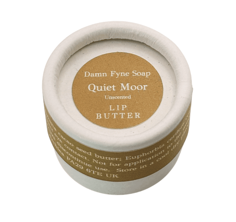 Quiet Moor Lip Butter in a biodegradable cylindrical container with a soft neutral label. Label reads “Damn Fyne Soap – Quiet Moor – Unscented – Lip Butter.” Photographed from above on a white background, showing the lid and part of the container.