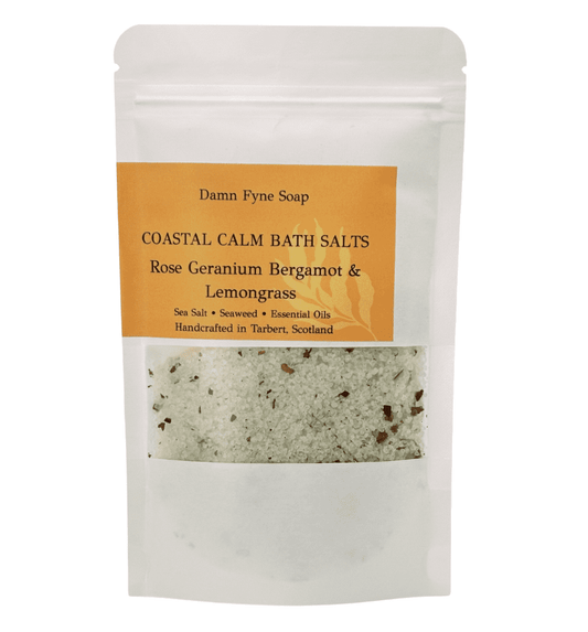 Coastal Calm Bath Salts in a semi-transparent kraft pouch with an orange label. Label reads “Coastal Calm Bath Salts – Rose Geranium, Bergamot & Lemongrass – Sea Salt • Seaweed • Essential Oils – Handcrafted in Tarbert, Scotland.” Contents visible through window, showing coarse salt and flecks of seaweed