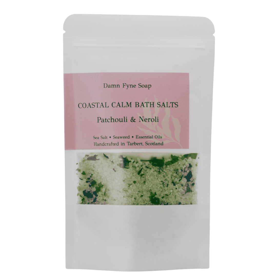 Coastal Calm Bath Salts in a semi-transparent kraft pouch with a soft pink label. Label reads “Coastal Calm Bath Salts – Patchouli & Neroli – Sea Salt + Seaweed + Essential Oils – Handcrafted in Tarbert, Scotland.” Contents visible through window, showing coarse green and white bath salts with flecks of seaweed