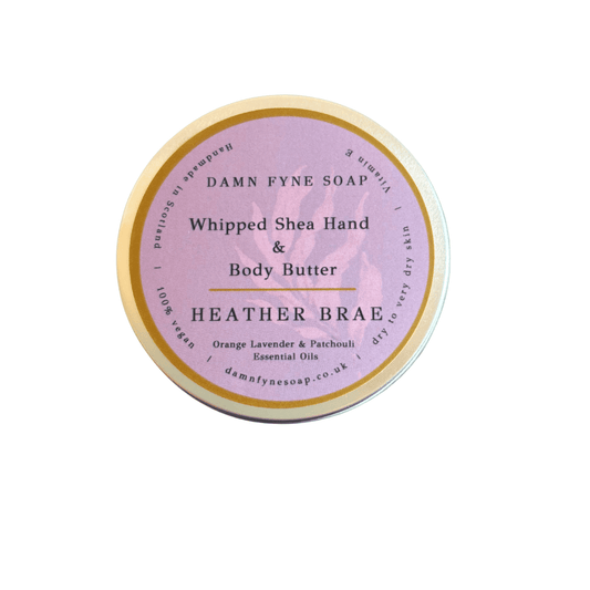 Lavender and gold-labeled container of Damn Fyne Soap’s Heather Brae Whipped Shea Hand & Body Butter, scented with orange, lavender, and patchouli essential oils. Handmade in Scotland.