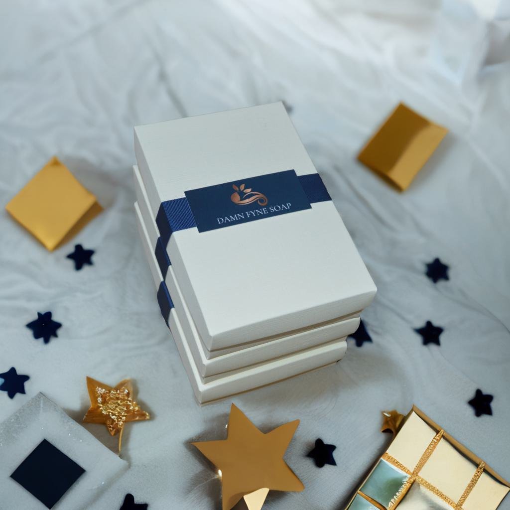 Elegant cream gift box from Damn Fyne Soap tied with dark blue ribbon, containing a trio of artisanal soaps in patchouli-based blends, styled with festive natural decorations.