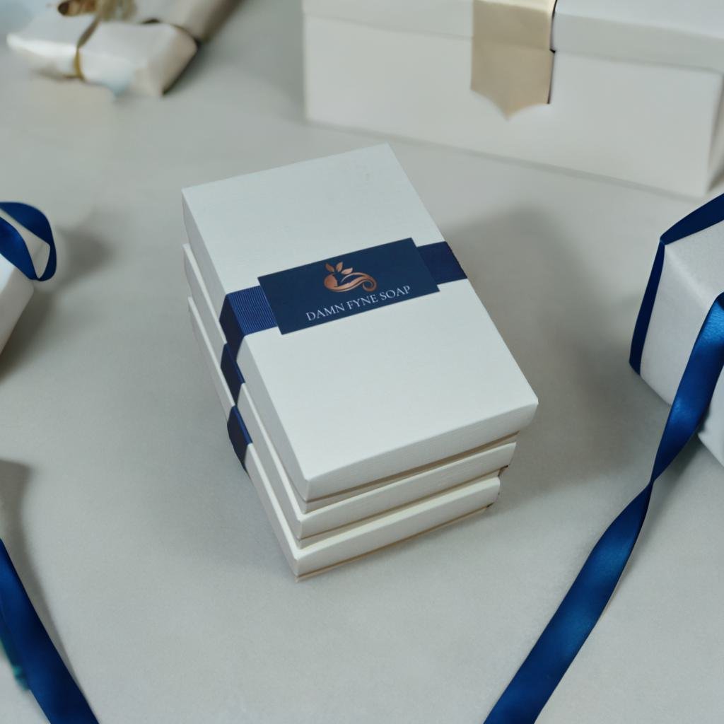Stack of three cream-colored Damn Fyne Soap gift boxes tied with dark blue ribbon, featuring elegant packaging and a branded label. Ideal for festive gifting or retail display.
