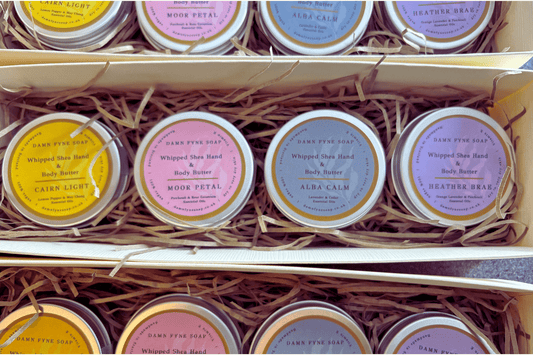Cream Damn Fyne Soap gift box with navy ribbon, containing four tins of whipped shea body butter—Cairn Light, Moor Petal, Heather Brae & Alba Calm— a seasonal, Christmas-ready presentation.