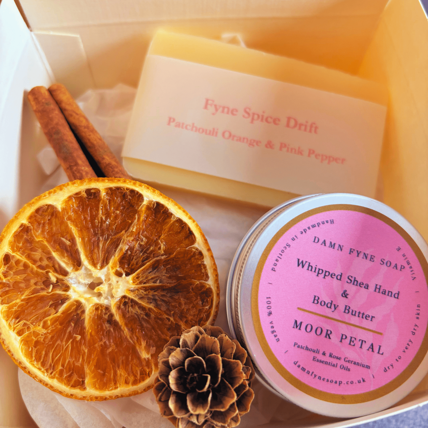 Cream gift box with navy ribbon, containing guest-size Fyne Spice Drift soap and Moor Petal whipped body butter. Styled with dried orange slice for seasonal presentation 