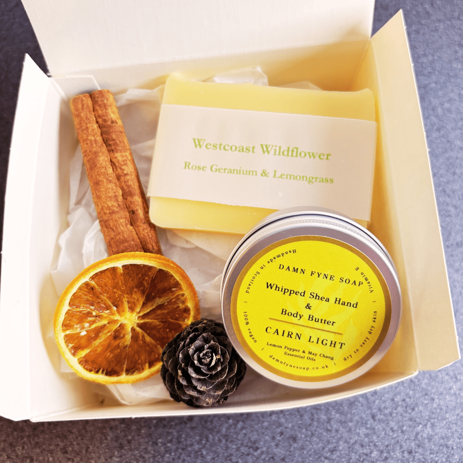 Cream gift box with navy ribbon, containing Westcoast Wildflower soap and Cairn Light body butter. Styled with seasonal elements like dried orange slice