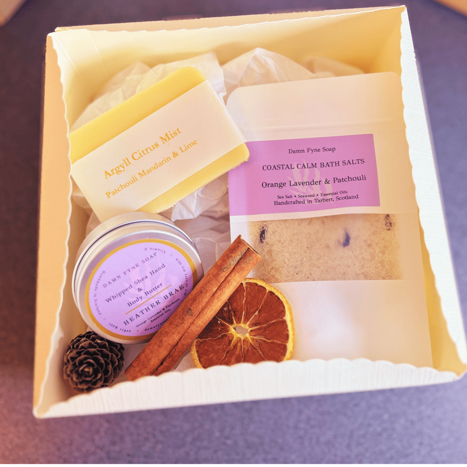 Cream gift box with navy ribbon, containing Argyll Citrus Mist guest soap, Heather Brae body butter, and Coastal Calm bath salts with orange, lavender & patchouli. Styled with dried orange slice