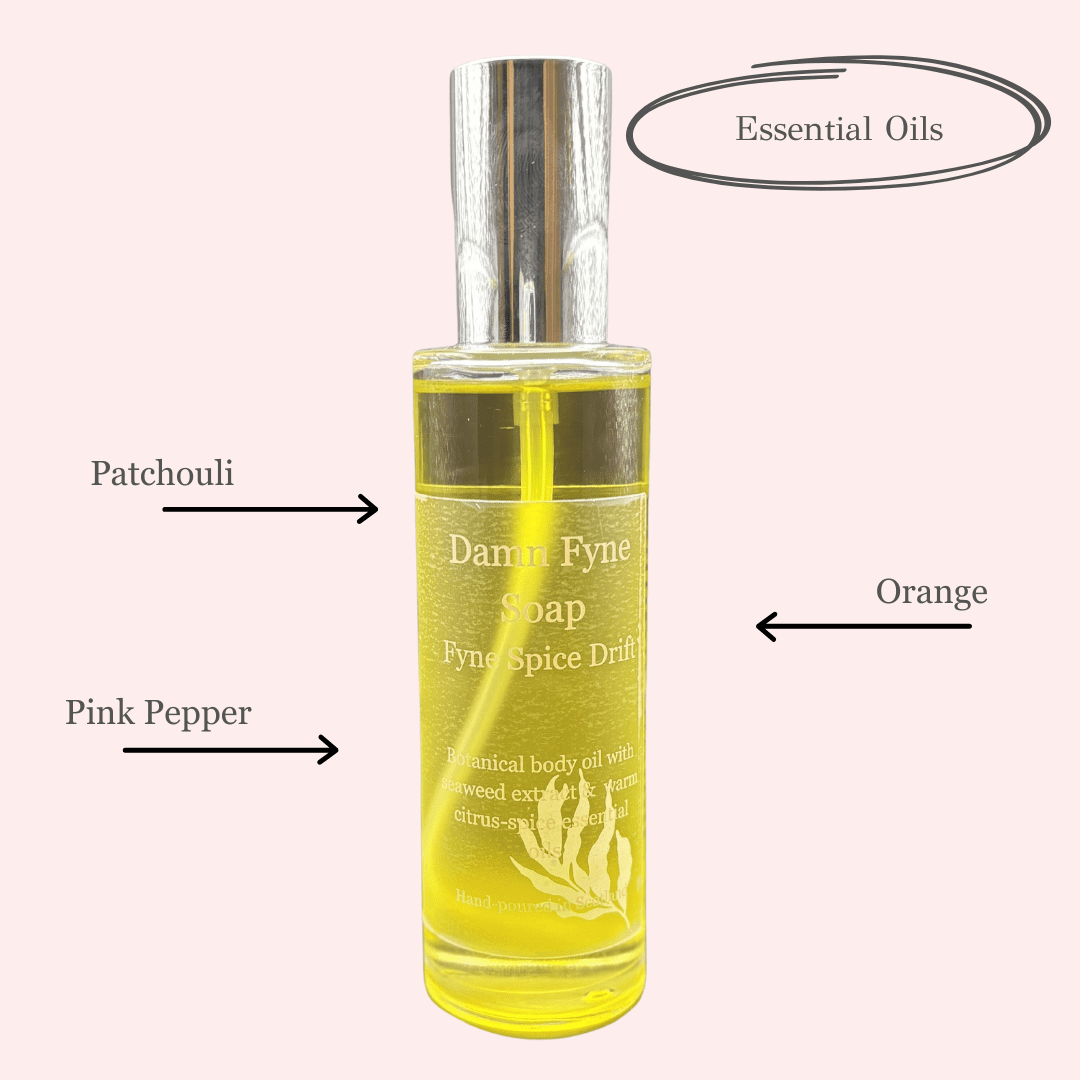Fyne Spice Drift body oil in a transparent bottle with warm golden oil inside. The pink text on the clear label describes a spiced citrus blend of patchouli, orange, and pink pepper essential oils. 