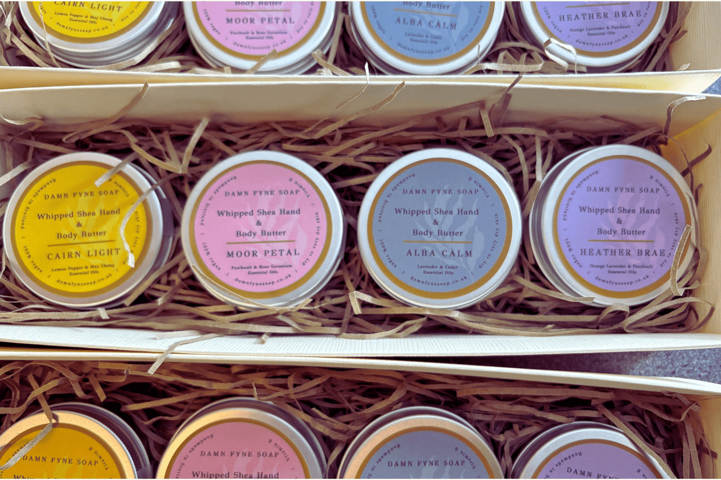 Cream Damn Fyne Soap gift box with navy ribbon, containing four tins of whipped shea body butter—Cairn Light, Moor Petal, Heather Brae & Alba Calm— 