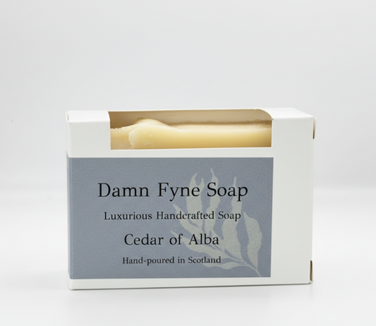 Cedar of Alba soap bar in biodegradable kraft packaging with a grey  label. Label reads “Damn Fyne Soap – Luxurious Handcrafted Soap – Cedar of Alba – Hand-poured in Scotland.” Light-toned soap visible above the box, photographed on a neutral background. lavender and cedarwood essential oils.