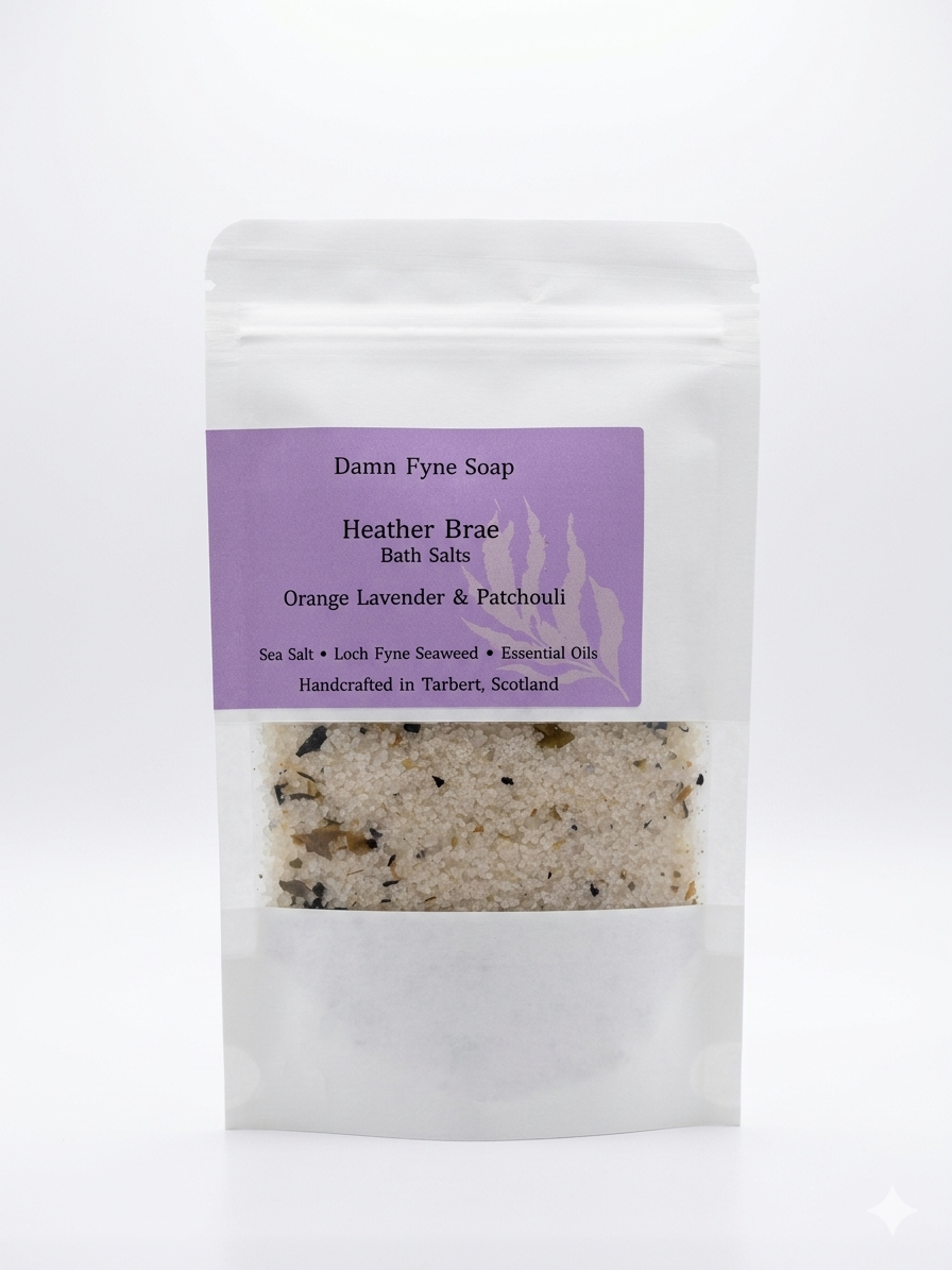 Bath Salts in a semi-transparent kraft pouch with a purple label. Label reads “Coastal Calm Bath Salts – Orange, Lavender & Patchouli – Sea Salt • Loch Fyne Seaweed • Essential Oils – Handcrafted in Tarbert, Scotland.” Contents visible through window, showing coarse salt and botanical elements.