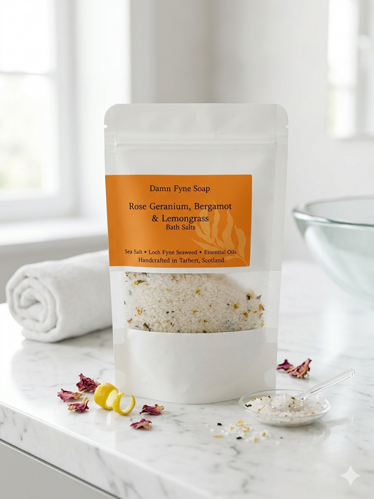 Bath Salts in a semi-transparent kraft pouch with an orange label. Label reads “Coastal Calm Bath Salts – Rose Geranium, Bergamot & Lemongrass – Sea Salt • Seaweed • Essential Oils – Handcrafted in Tarbert, Scotland.” Contents visible through window, showing coarse salt and flecks of seaweed