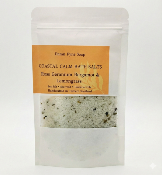 Coastal Calm Bath Salts in a semi-transparent kraft pouch with an orange label. Label reads “Coastal Calm Bath Salts – Rose Geranium, Bergamot & Lemongrass – Sea Salt • Seaweed • Essential Oils – Handcrafted in Tarbert, Scotland.” Contents visible through window, showing coarse salt and flecks of seaweed